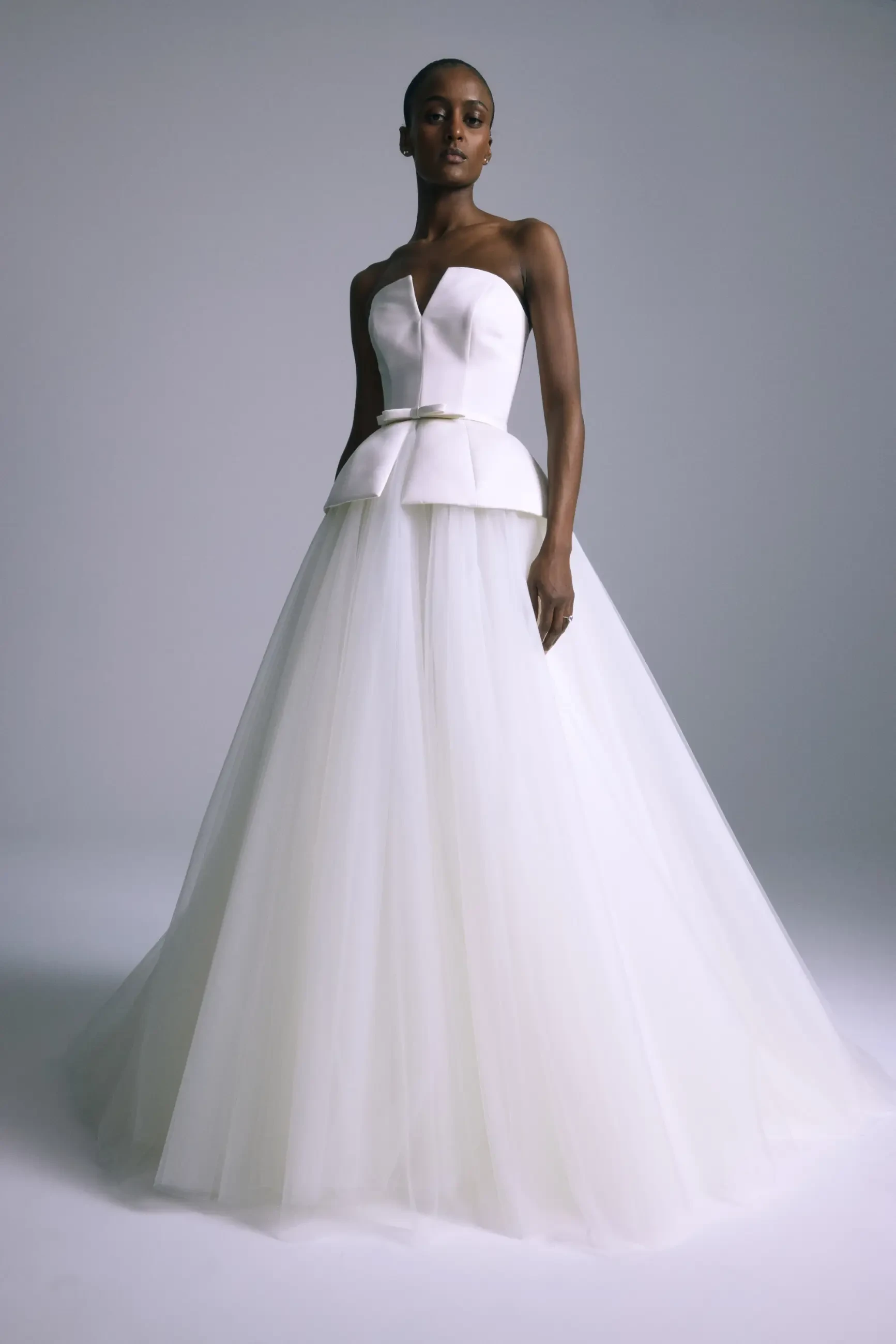 Model is wearing a structured peplum corset gown in Italian double-faced duchess satin with a tulle skirt and a high lace collar topper.
