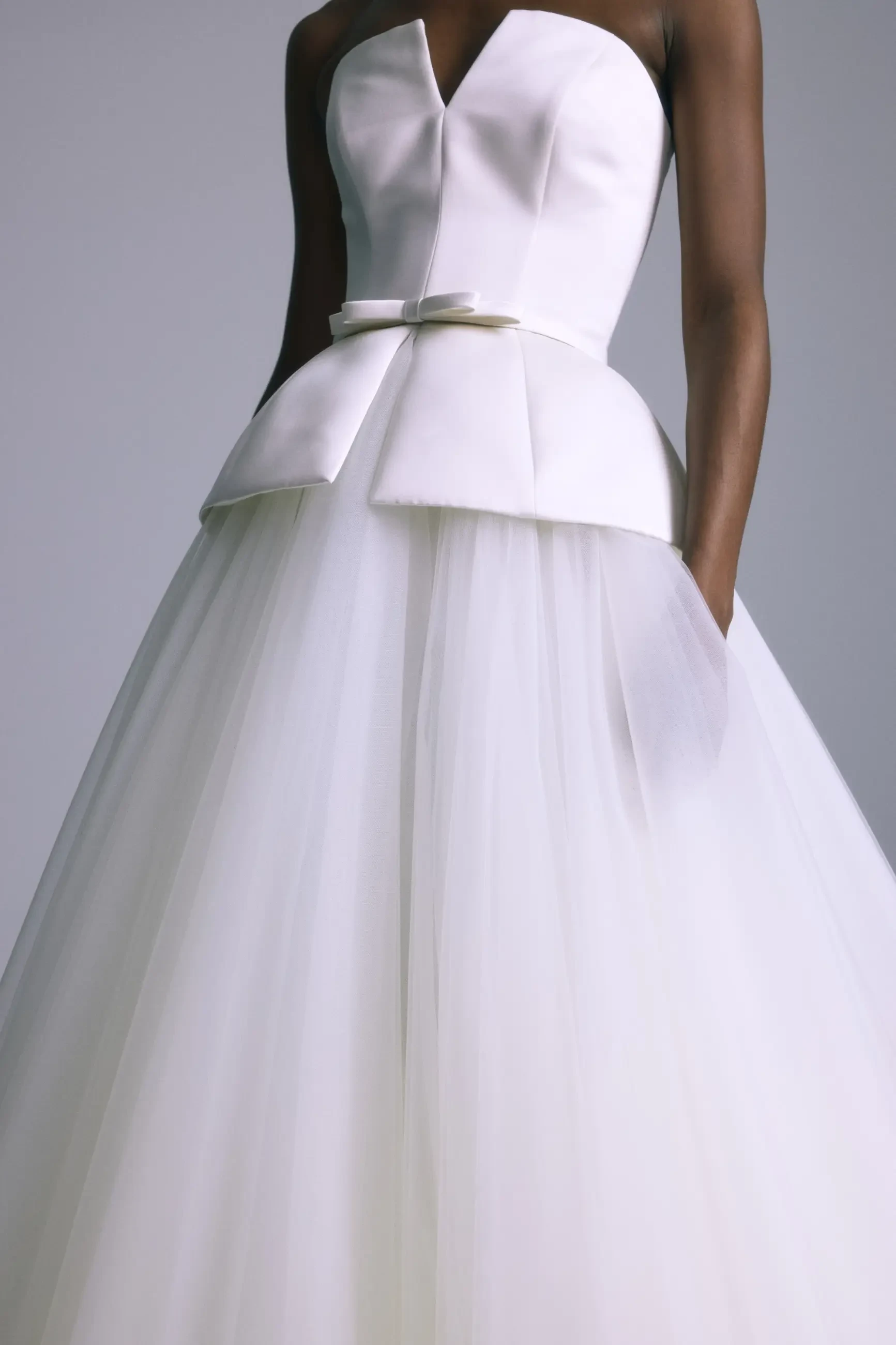 Model is wearing a structured peplum corset gown in Italian double-faced duchess satin with a tulle skirt and a high lace collar topper.