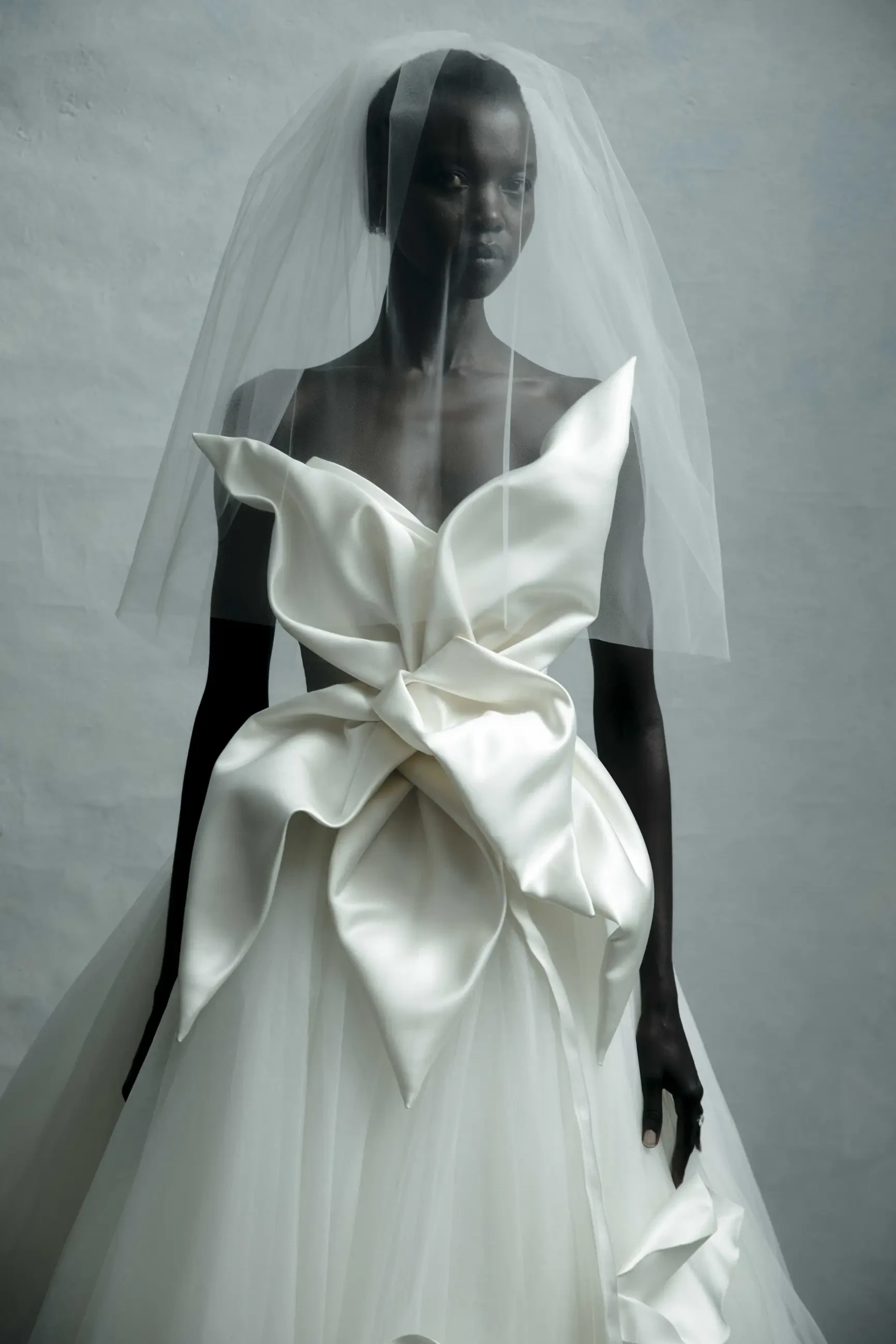 Model is wearing a taffeta and tulle ball gown with a ruched bodice and oversized 3D floral motif.