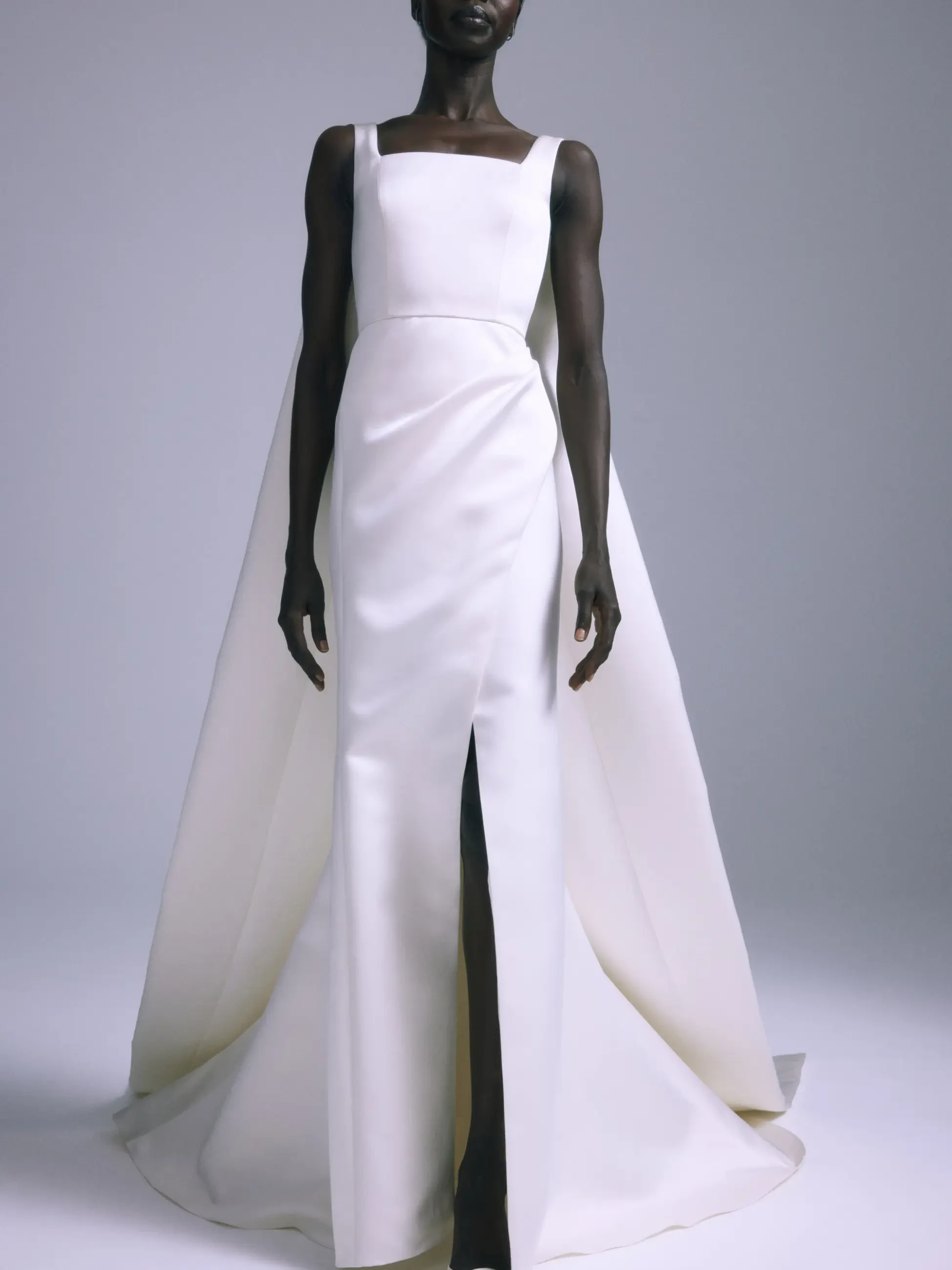 Model is wearing a U-neck fit-and-flare gown in Italian double-faced duchess satin, finished with a dramatic cape and bow.