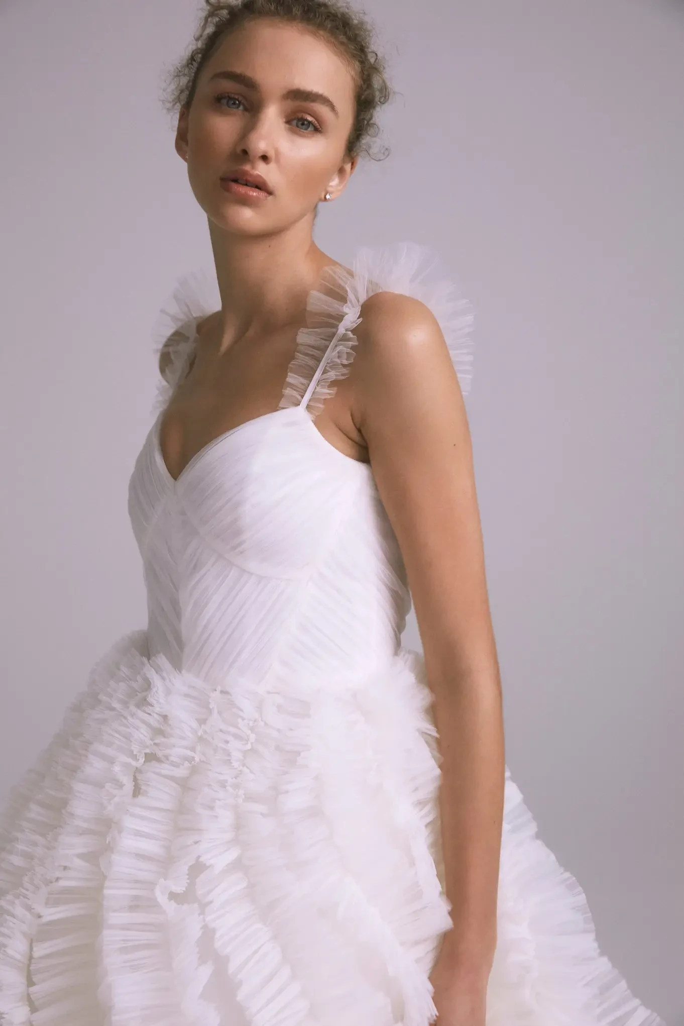 Model is wearing a ruched tulle cami bodice paired with a voluminous mushroom-pleated ruffle ball gown.