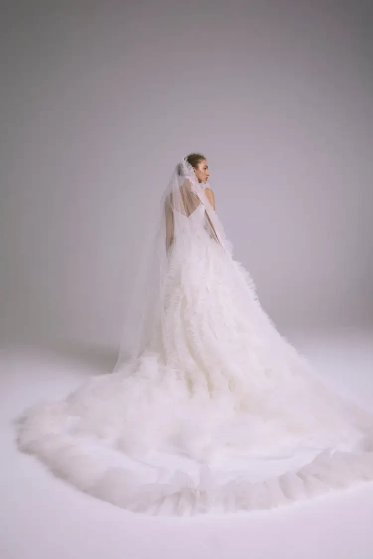 Model is wearing a ruched tulle cami bodice paired with a voluminous mushroom-pleated ruffle ball gown.