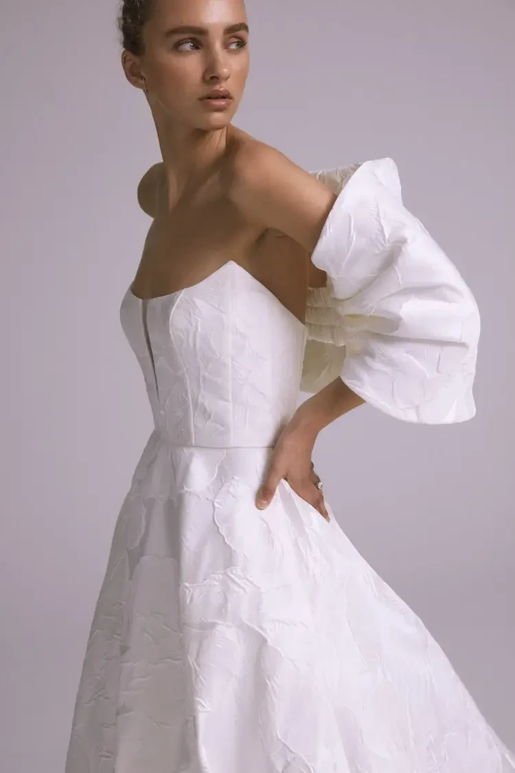 Model is wearing a strapless blooming floral jacquard gown with an illusion plunge cutaway.