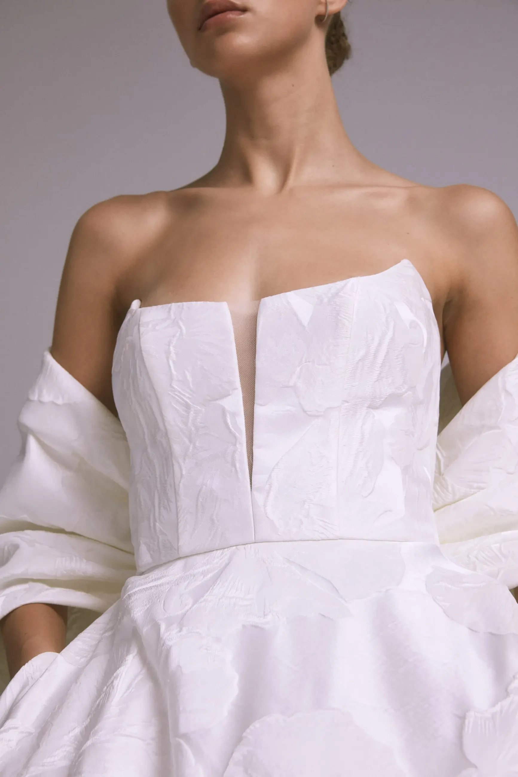 Model is wearing a strapless blooming floral jacquard gown with an illusion plunge cutaway.