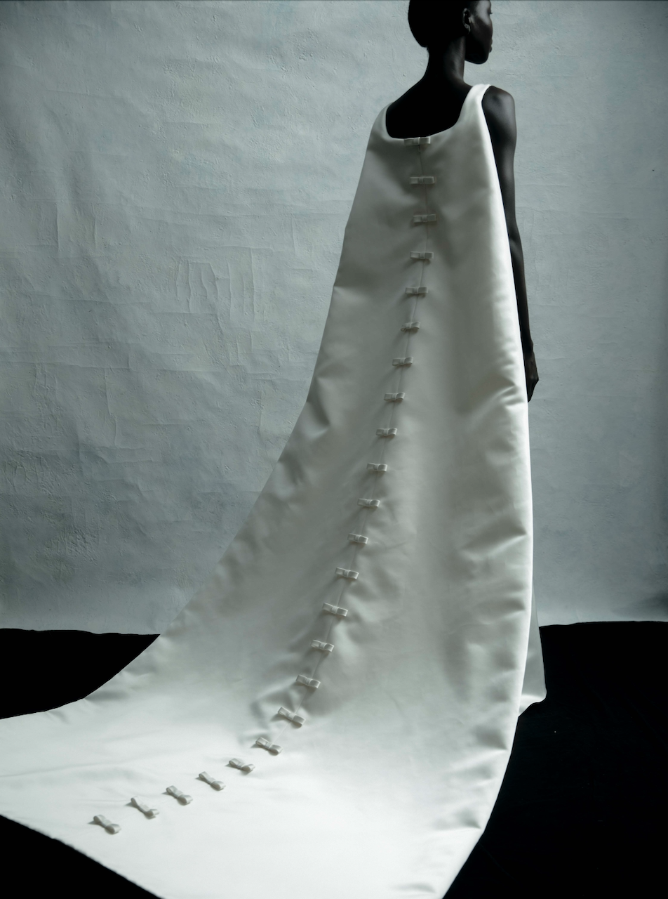 Model is wearing a U-neck fit-and-flare gown in Italian double-faced duchess satin, finished with a dramatic cape and bow.
