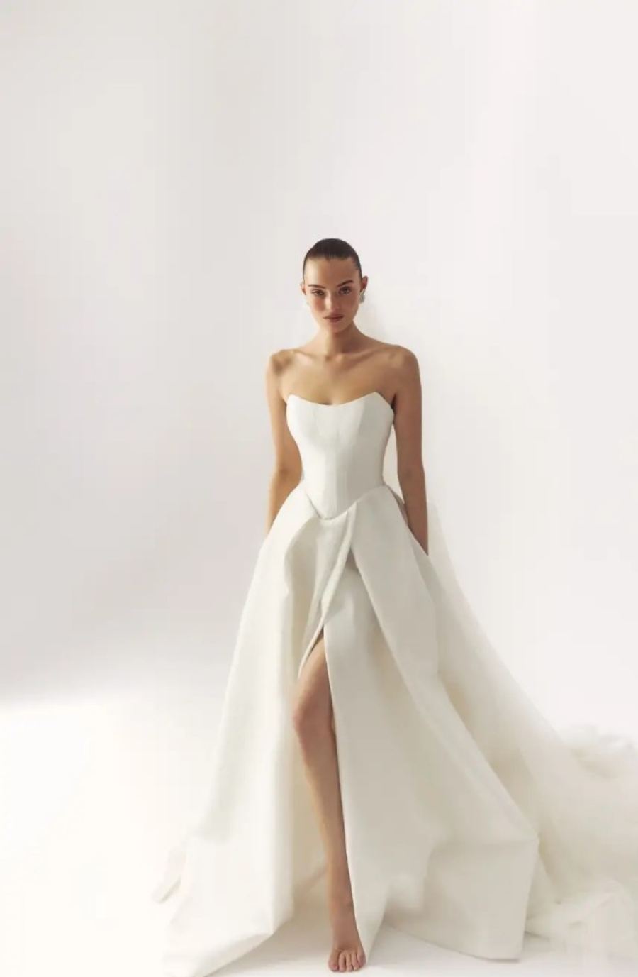 Model is wearing a strapless ball gown with a scoop neckline and high slit with dropped waist by lihi hod