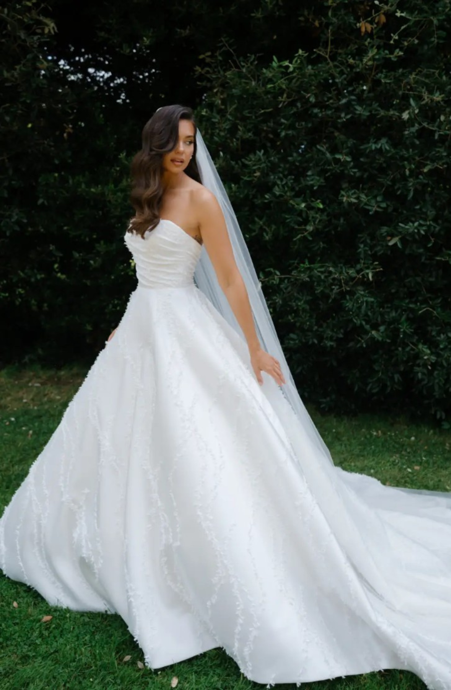 Model is wearing a strapless ball gown with a ruched fitted bodice and embroidered full skirt by suzanne neville